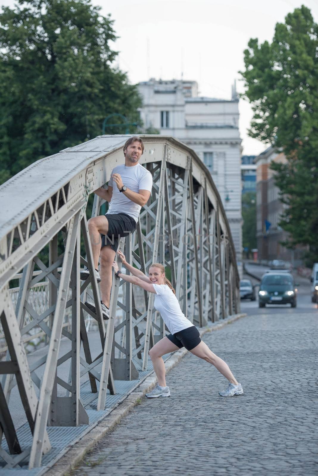 jogging couple warming up and stretching before morning running training workout  in the city with sunrise in background