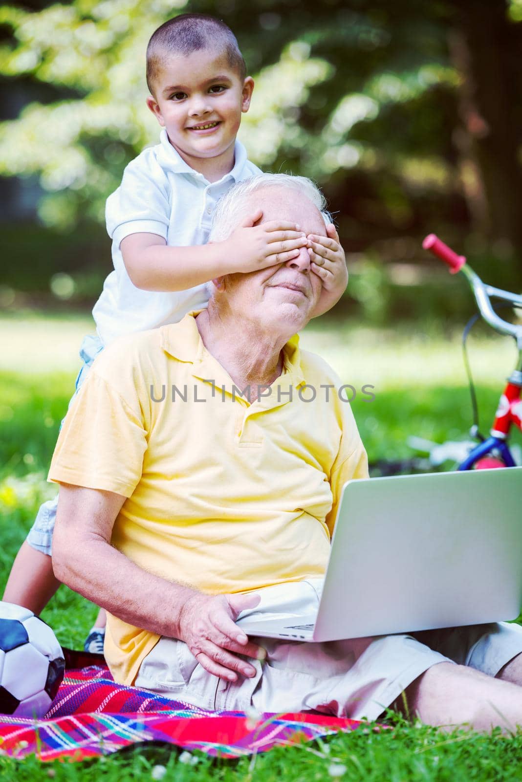 happy elderly senior grandfather and child in park using laptop computer