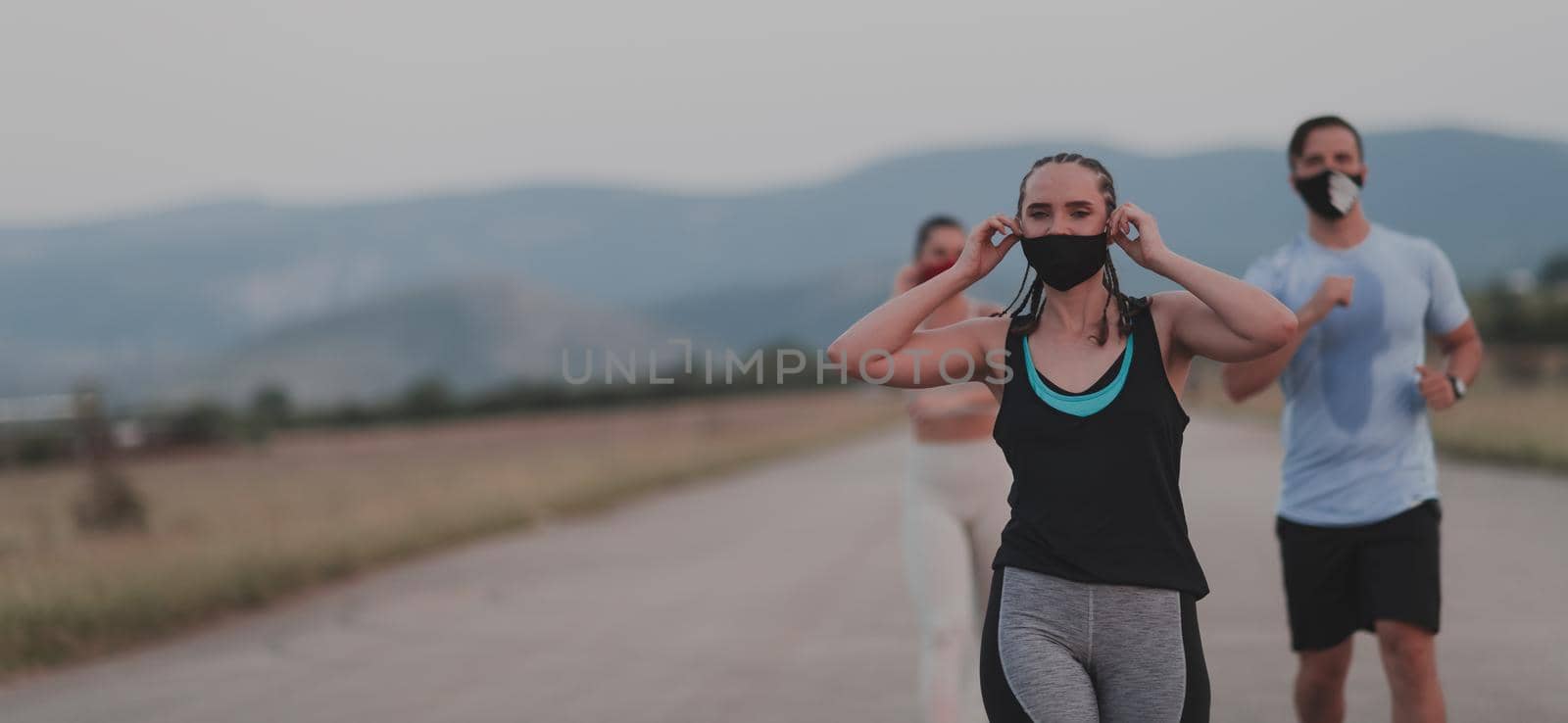 Multiethnic runners group wear face masks running keep social distance outdoor. Fit healthy diverse team wears sportswear jogging in evening on nature sports track distancing for safety. by dotshock