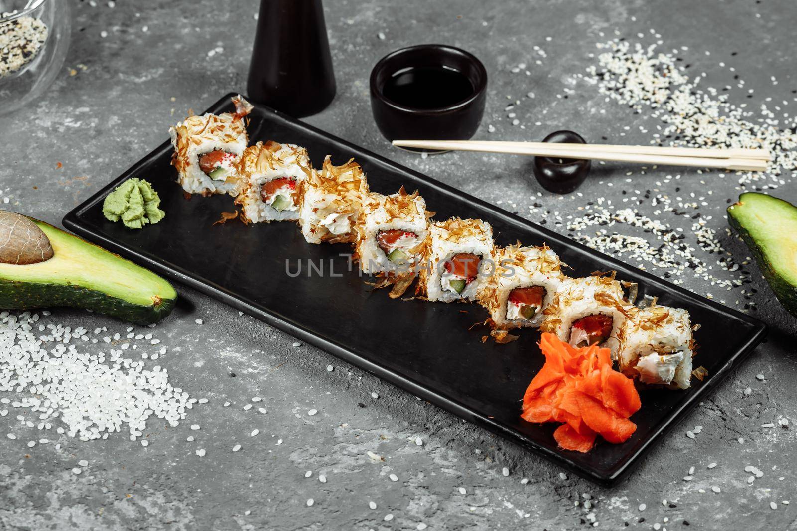 sushi rolls with cream cheese, fried salmon, tuna shavings or dried bonito, cucumber, nori. Chopsticks holding fresh katsuobushi roll in Japanese restaurant closeup.