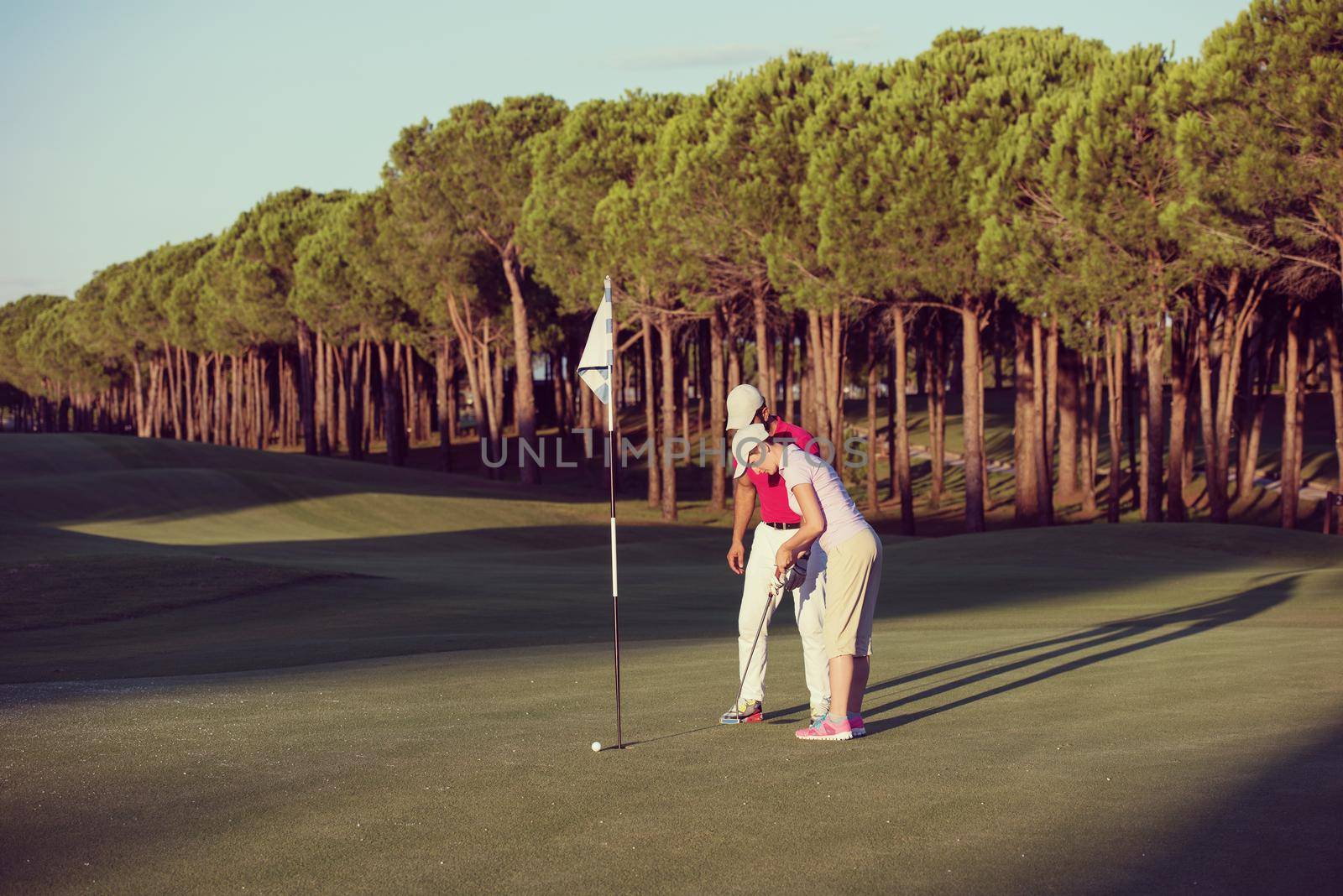 male golf instructor teaching female golf player, personal trainer giving lesson on golf course