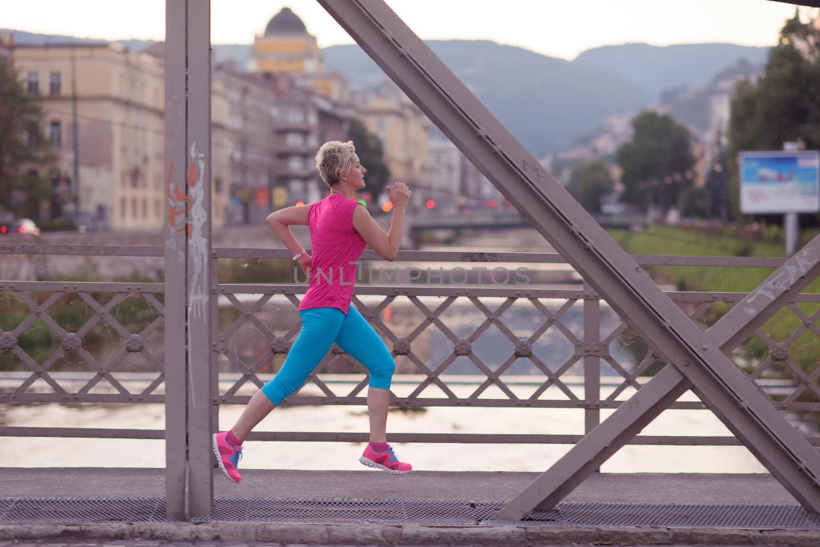 sporty woman running on sidewalk at early morning with city  sunrise scene in background