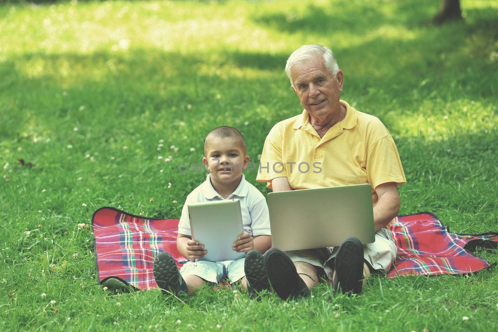 happy elderly senior grandfather and child in park using laptop computer