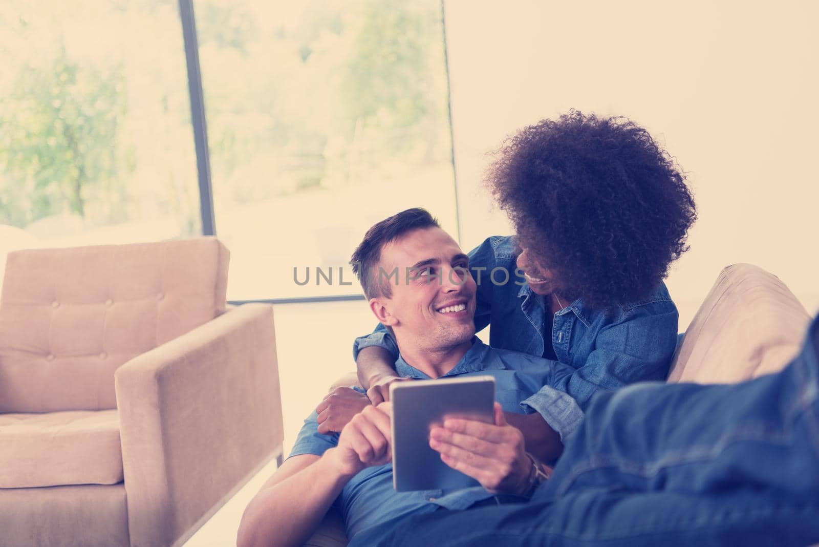 Young multiethnic couple relaxing at luxurious home with tablet computers reading in the living room on the sofa couch.