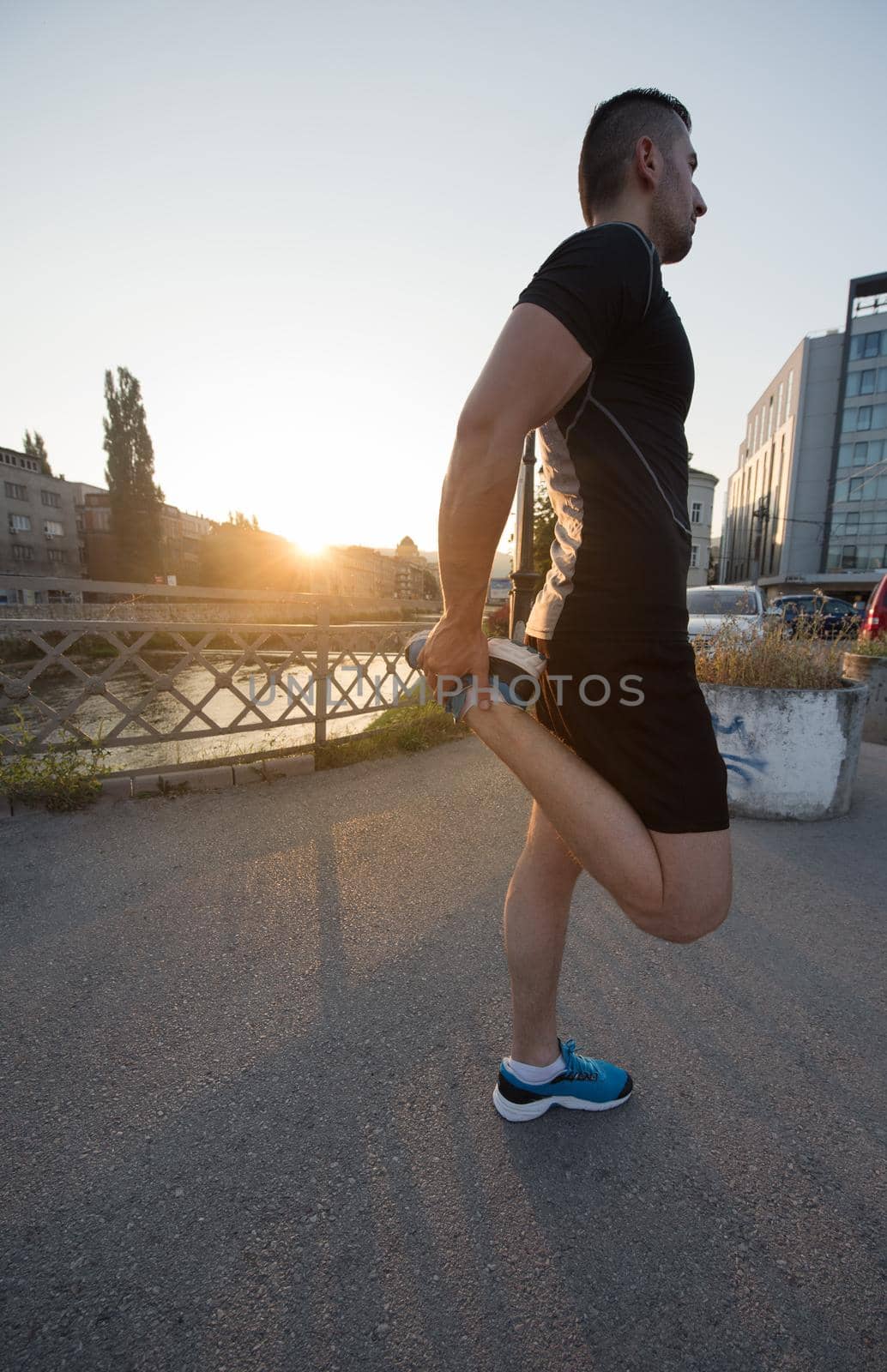 athlete man warming up and stretching while preparing for running on the city street at  sunny morning