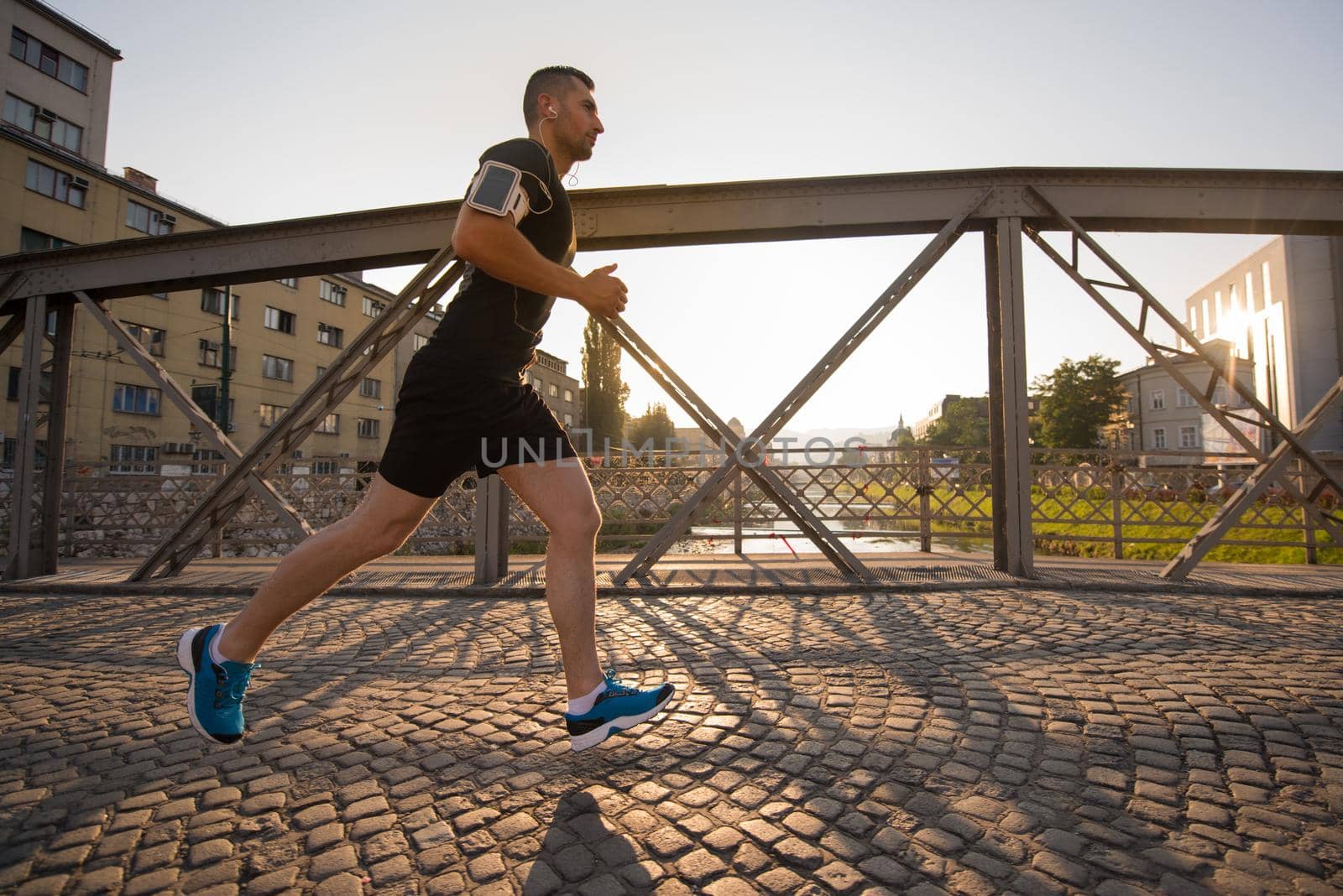 young sporty man jogging across the bridge at sunny morning in the city