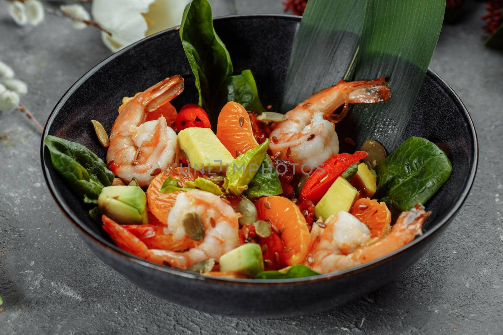 Shrimps salad with cherry tomatoes, cucumeber, avocado, lettuce and pomegranate on dish. Healthy seafood concept. Tasty grilled prawn shrimp and mix vegetable salad on black, top view by UcheaD