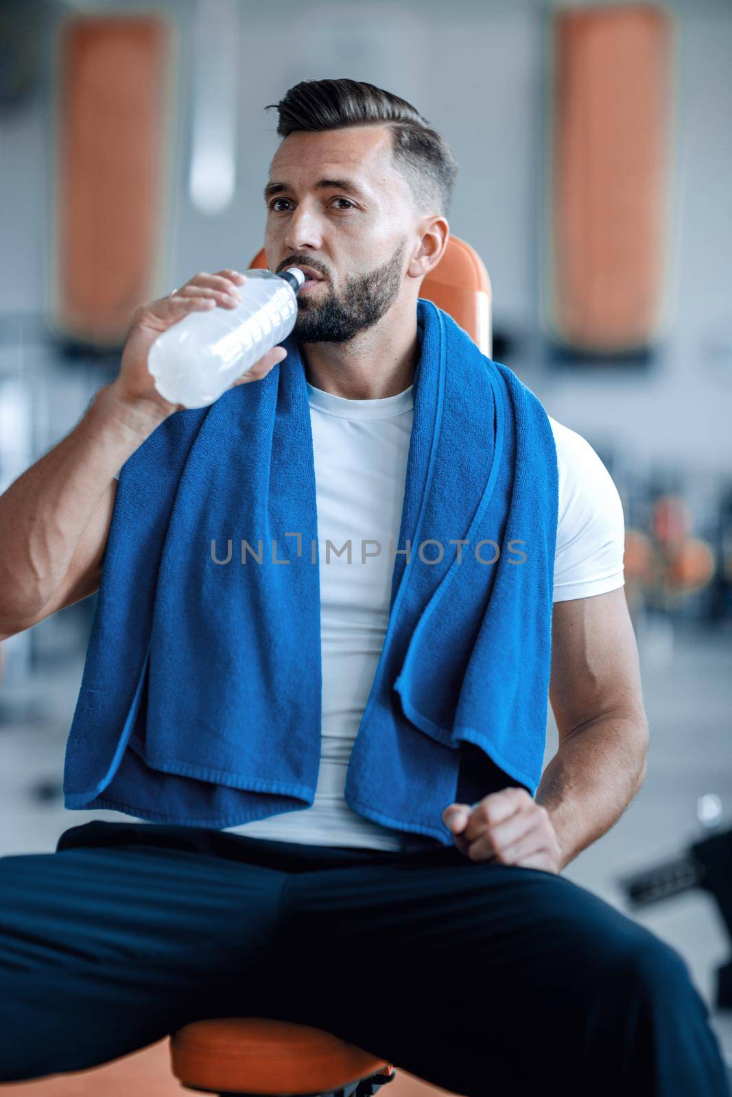 attractive man drinking bottled water in the gym. the concept of a healthy lifestyle