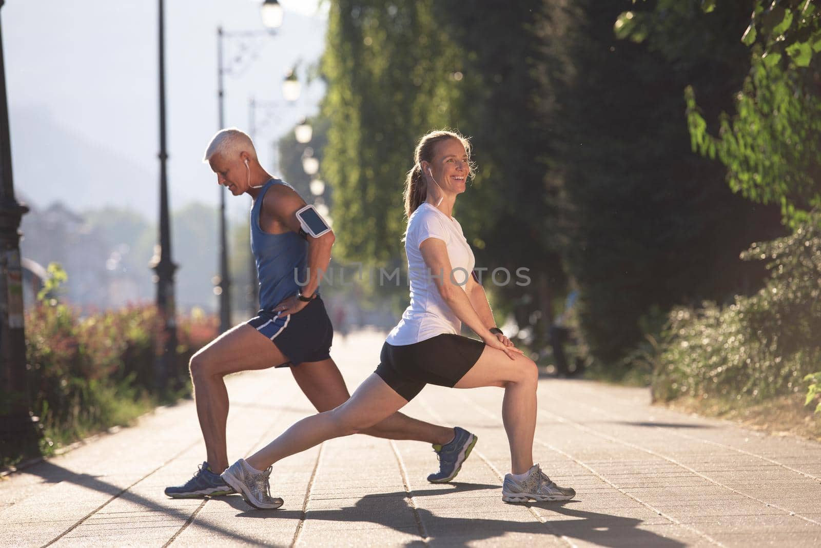 jogging couple warming up and stretching before morning running training workout  in the city with sunrise in background