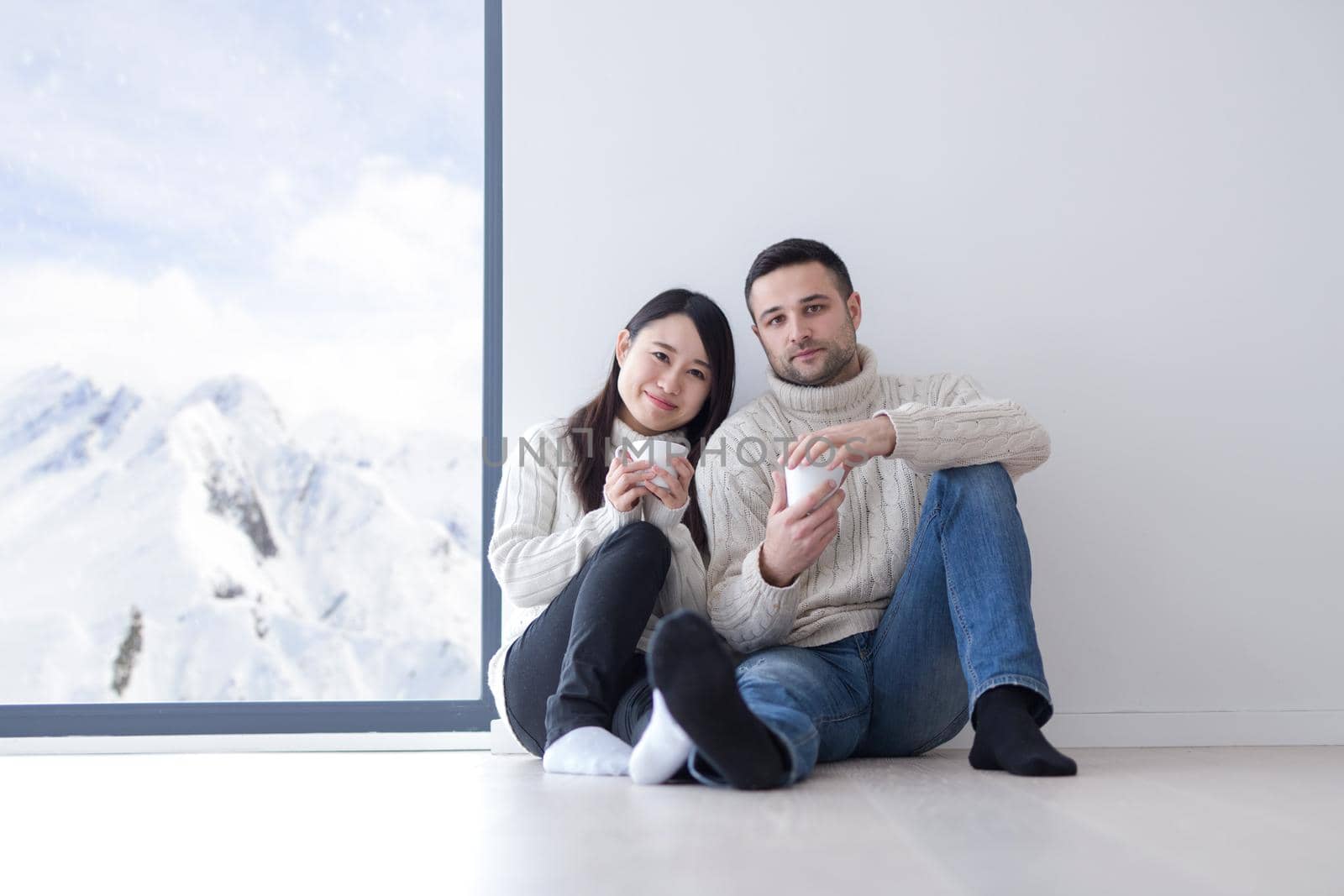 happy young multiethnic couple enjoying morning coffee by the window on cold winter day at home