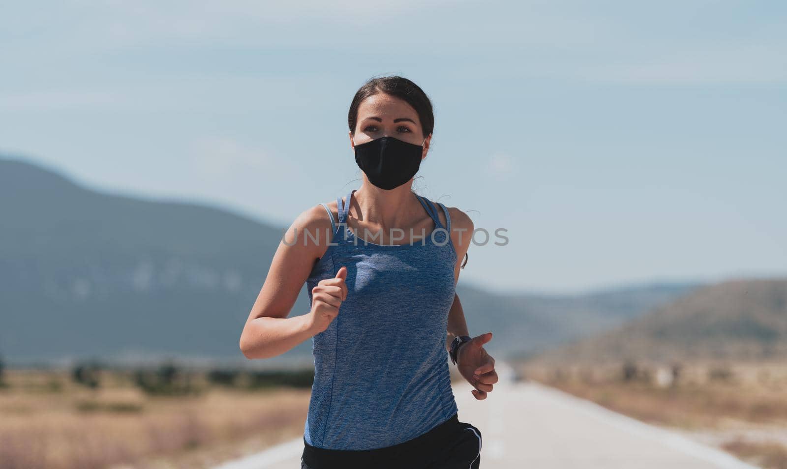 Determined fitness woman in short clothes wearing red protective face mask running outdoors in the city during coronavirus outbreak. Covid 19 and physical jogging activity, sport and fitness. by dotshock