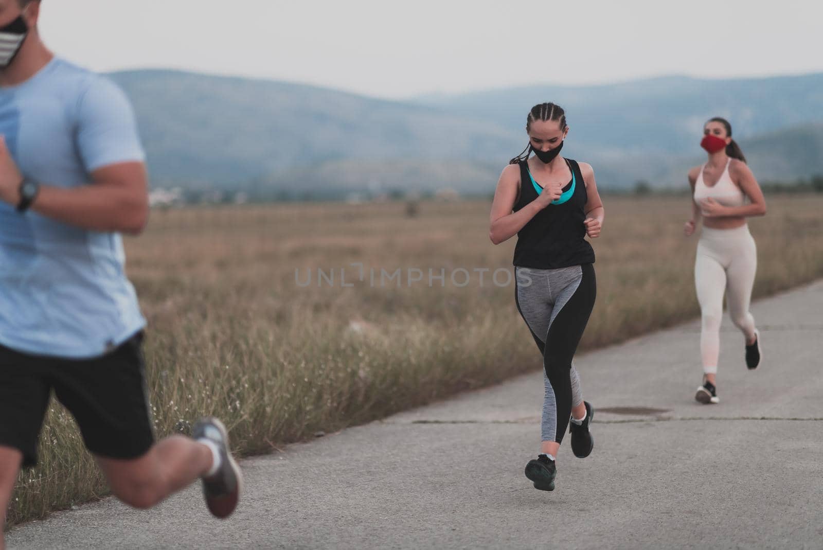 Three multiethnic women runners group wear face masks running keep social distance outdoor. Fit healthy diverse team wears sportswear jogging in park on nature sports track distancing for safety.