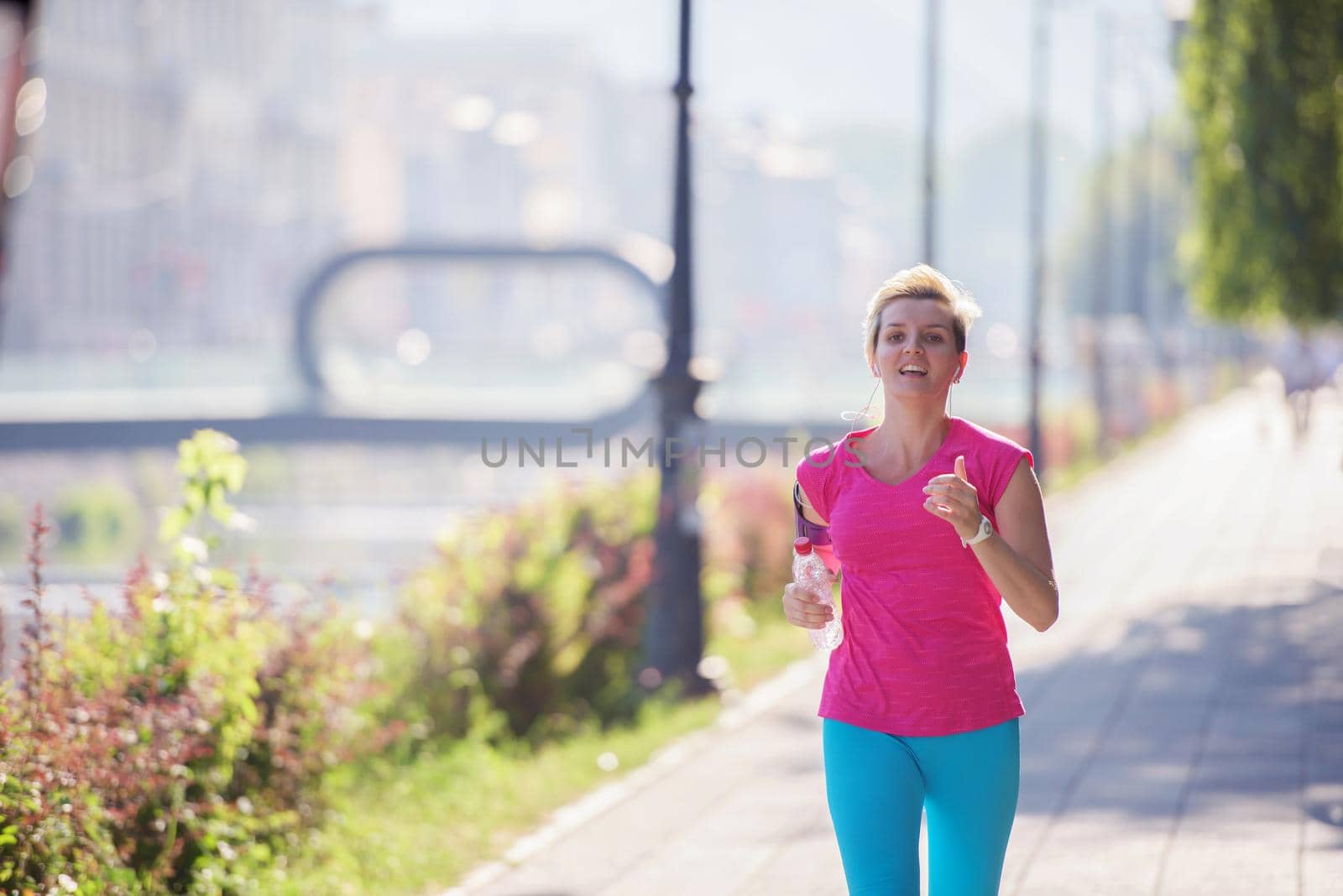 sporty woman running on sidewalk at early morning with city  sunrise scene in background