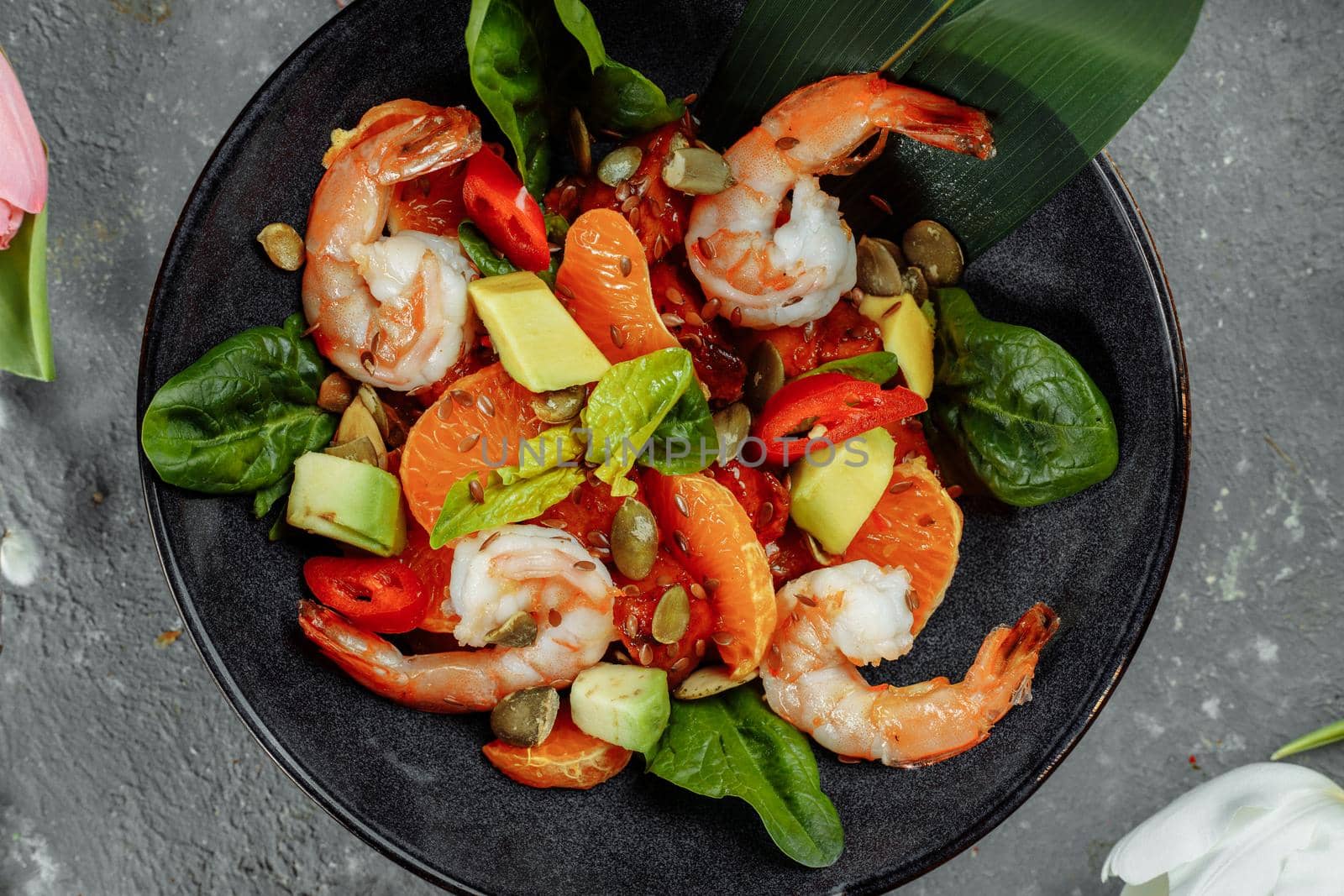 Shrimps salad with cherry tomatoes, cucumeber, avocado, lettuce and pomegranate on dish. Healthy seafood concept. Tasty grilled prawn shrimp and mix vegetable salad on black, top view by UcheaD