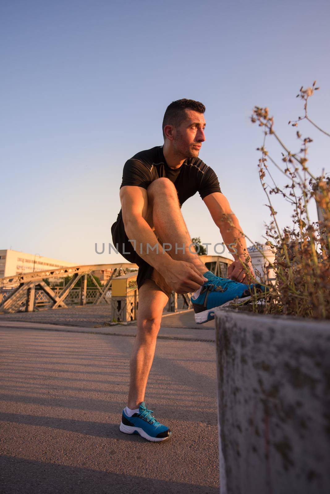 man tying running shoes laces getting ready to run on city at sunny morning