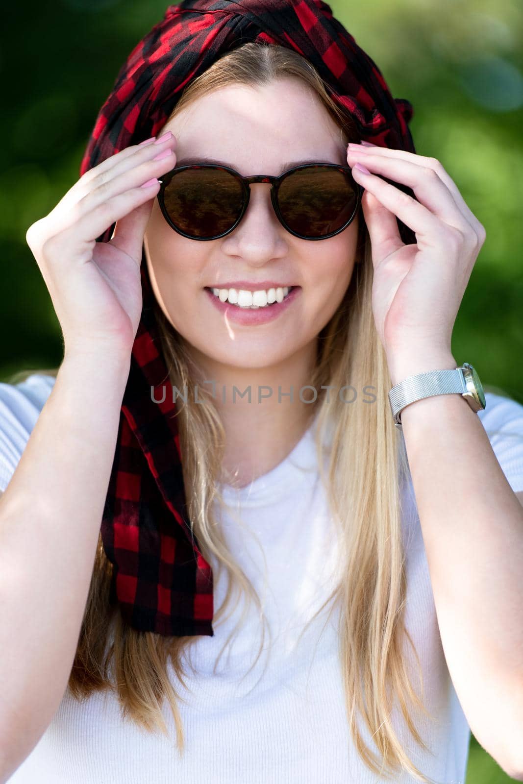 portrait of young smiling pretty girl with sunglasses and headscarf while standing in beautiful nature