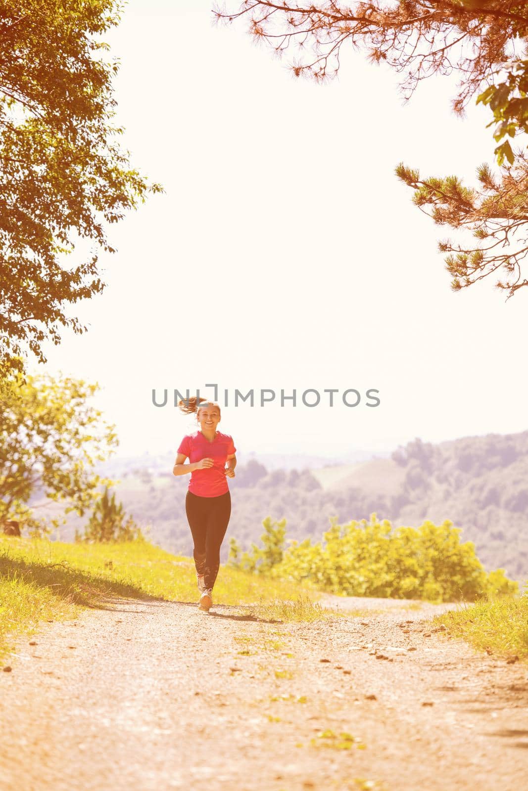 young happy woman enjoying in a healthy lifestyle while jogging on a country road through the beautiful sunny forest, exercise and fitness concept