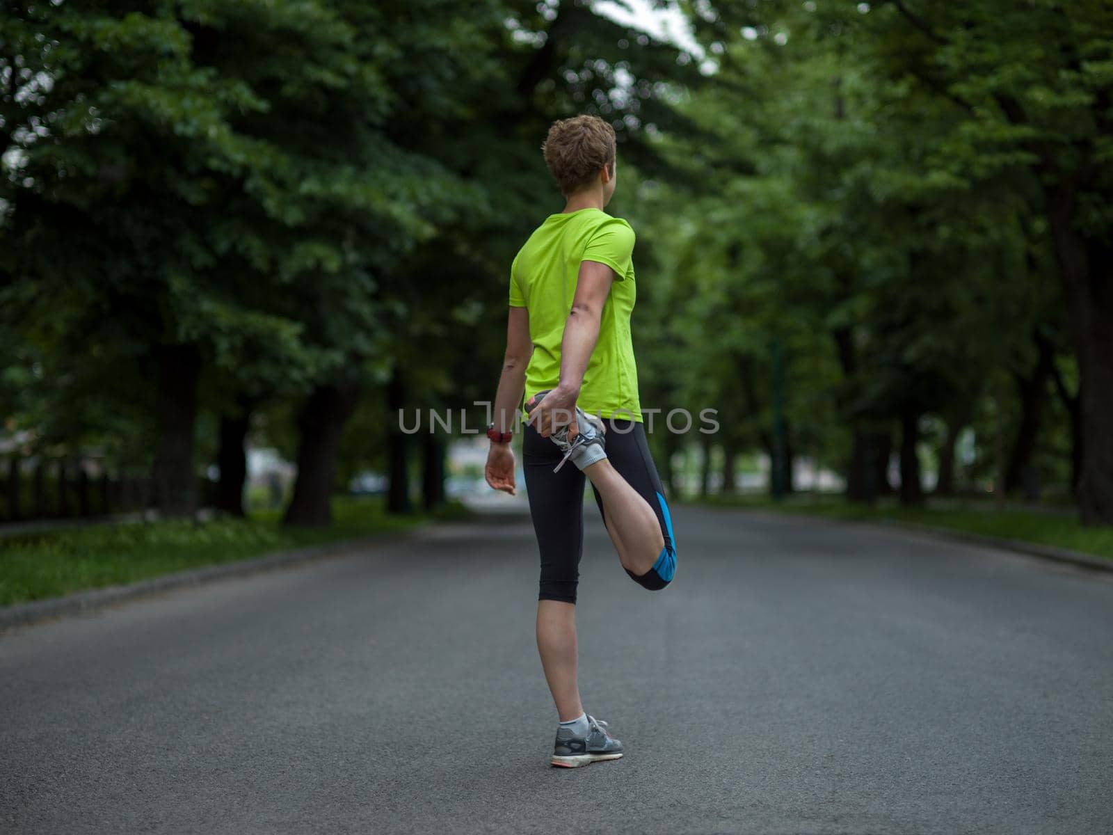 healthy female runner warming up and stretching in city park before morning training