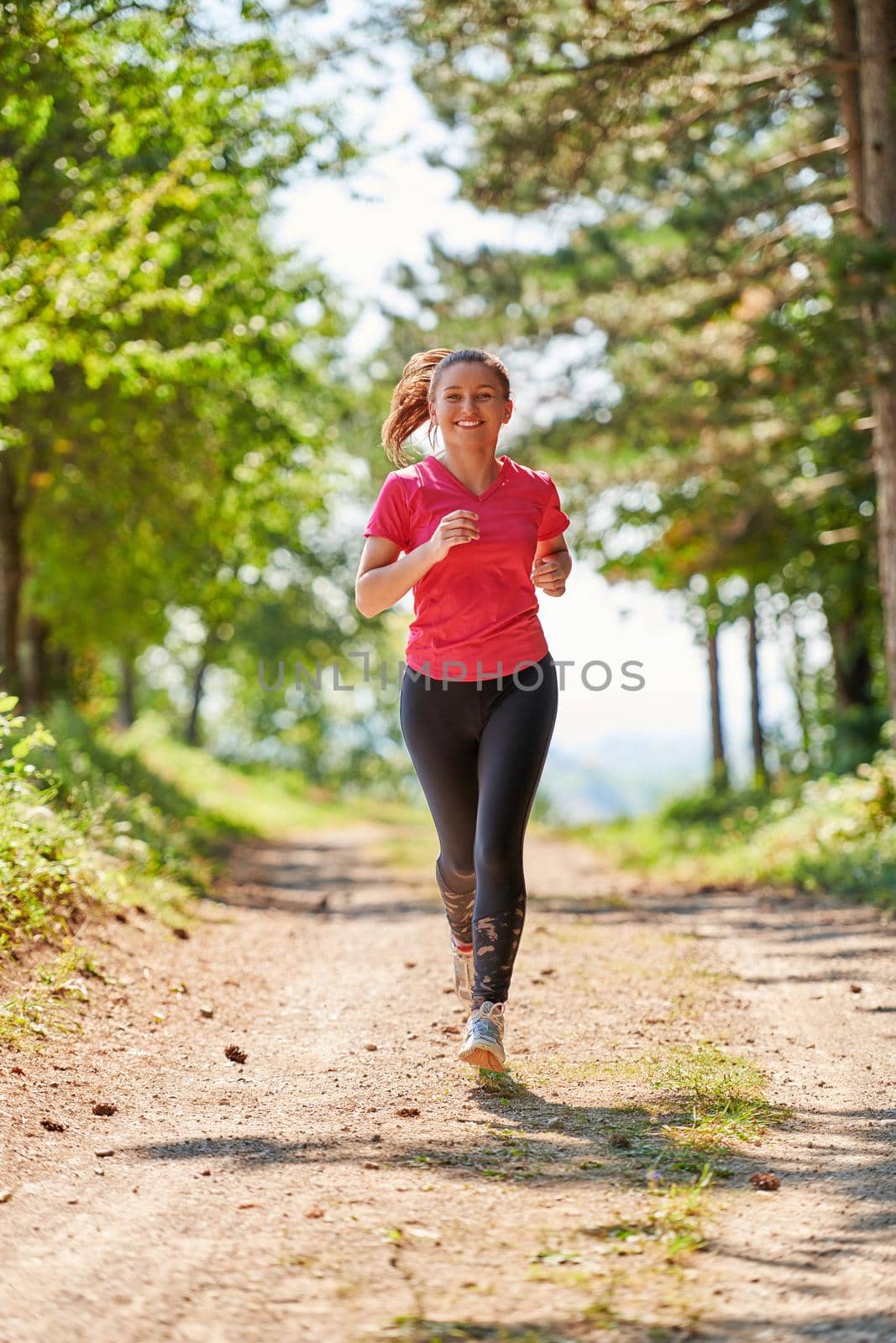 woman enjoying in a healthy lifestyle while jogging on a country road through the beautiful sunny forest, exercise and fitness concept