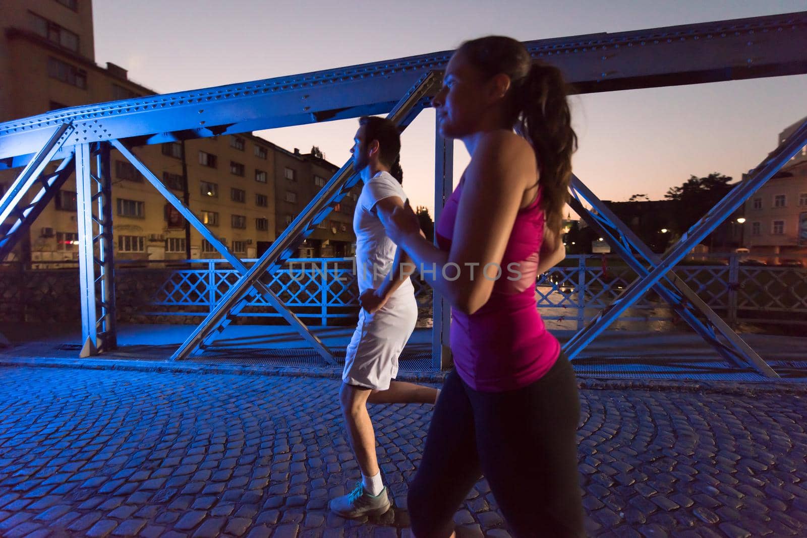 couple jogging across the bridge in the city by dotshock
