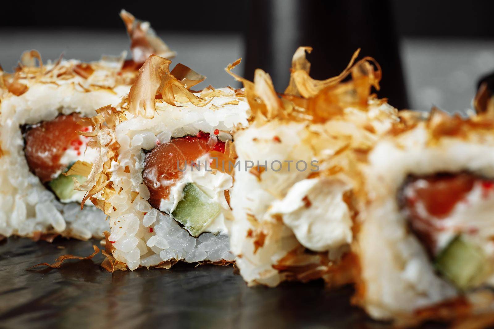 sushi rolls with cream cheese, fried salmon, tuna shavings or dried bonito, cucumber, nori. Chopsticks holding fresh katsuobushi roll in Japanese restaurant closeup by UcheaD