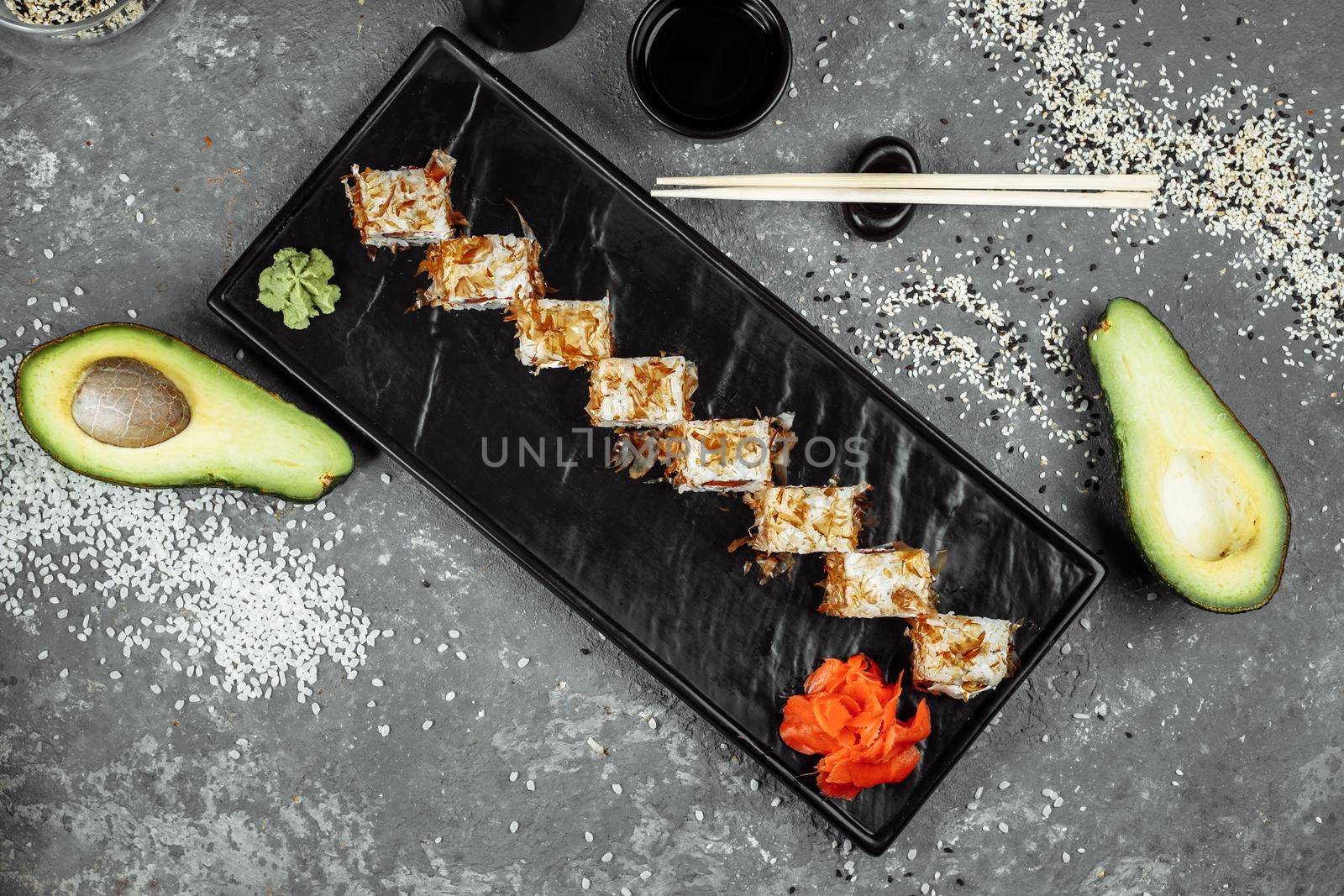 sushi rolls with cream cheese, fried salmon, tuna shavings or dried bonito, cucumber, nori. Chopsticks holding fresh katsuobushi roll in Japanese restaurant closeup by UcheaD