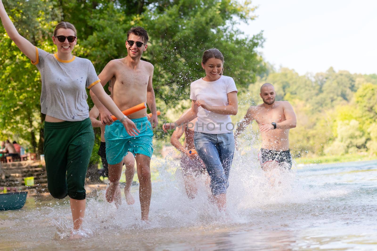 Summer joy group of happy friends having fun while running and splashing on river