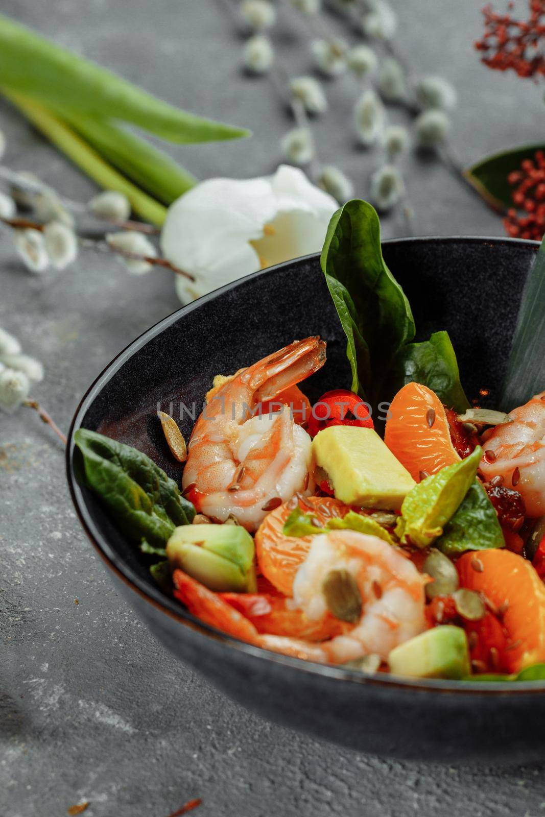 Shrimps salad with cherry tomatoes, cucumeber, avocado, lettuce and pomegranate on dish. Healthy seafood concept. Tasty grilled prawn shrimp and mix vegetable salad on black, top view.