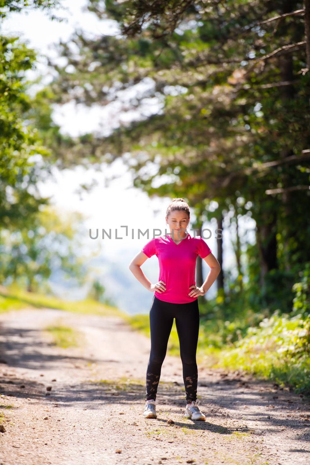 portyrait of young happy woman enjoying in a healthy lifestyle while jogging on a country road through the beautiful sunny forest, exercise and fitness concept