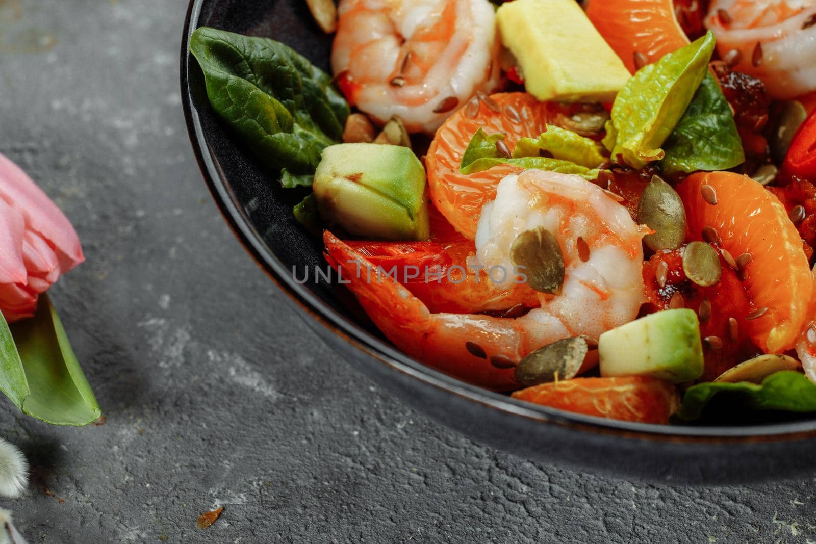 Shrimps salad with cherry tomatoes, cucumeber, avocado, lettuce and pomegranate on dish. Healthy seafood concept. Tasty grilled prawn shrimp and mix vegetable salad on black, top view by UcheaD