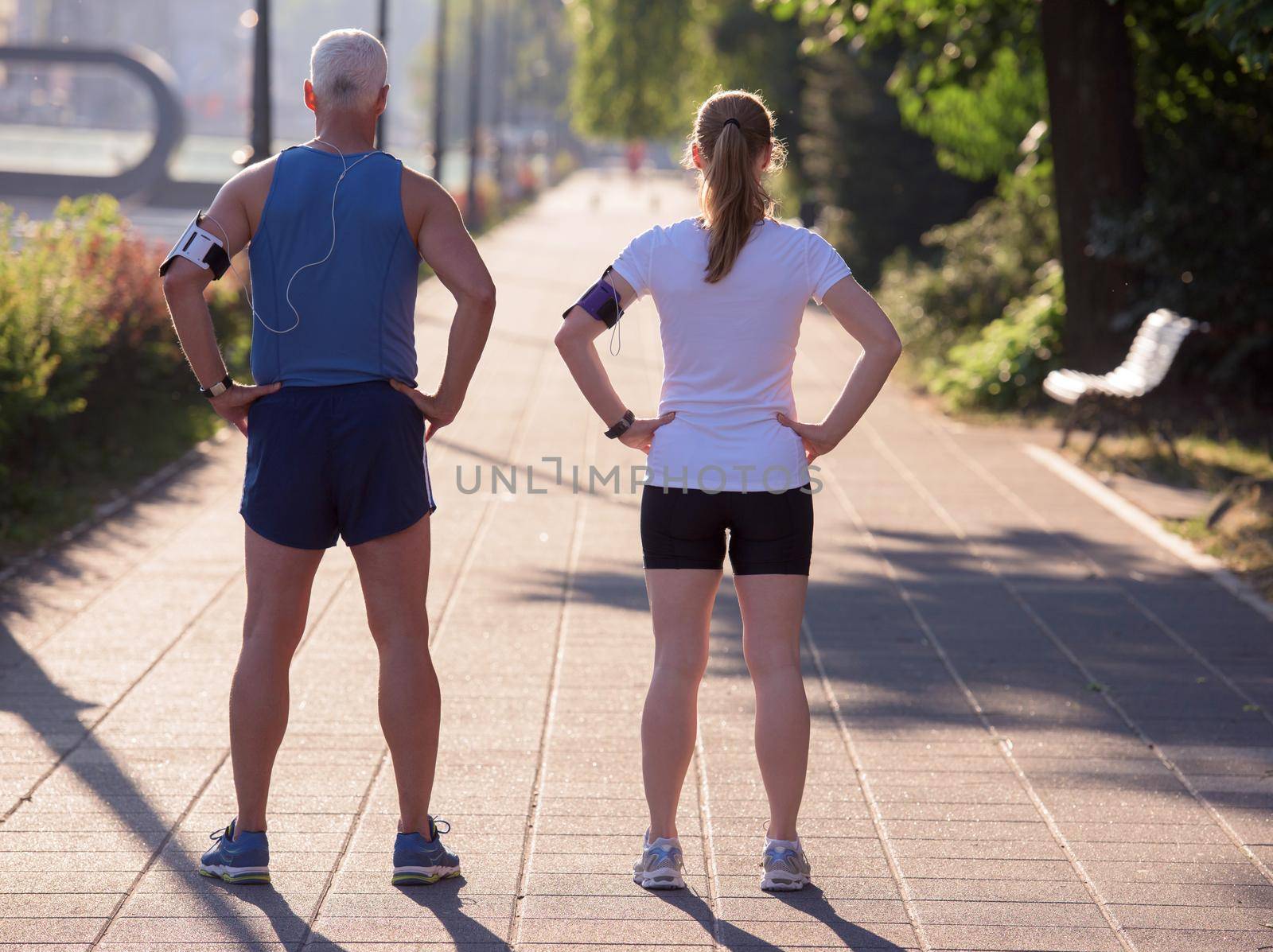 jogging couple check music playlist on phone and plan route before morning running workout  with sunrise in the city  and sun flare in background