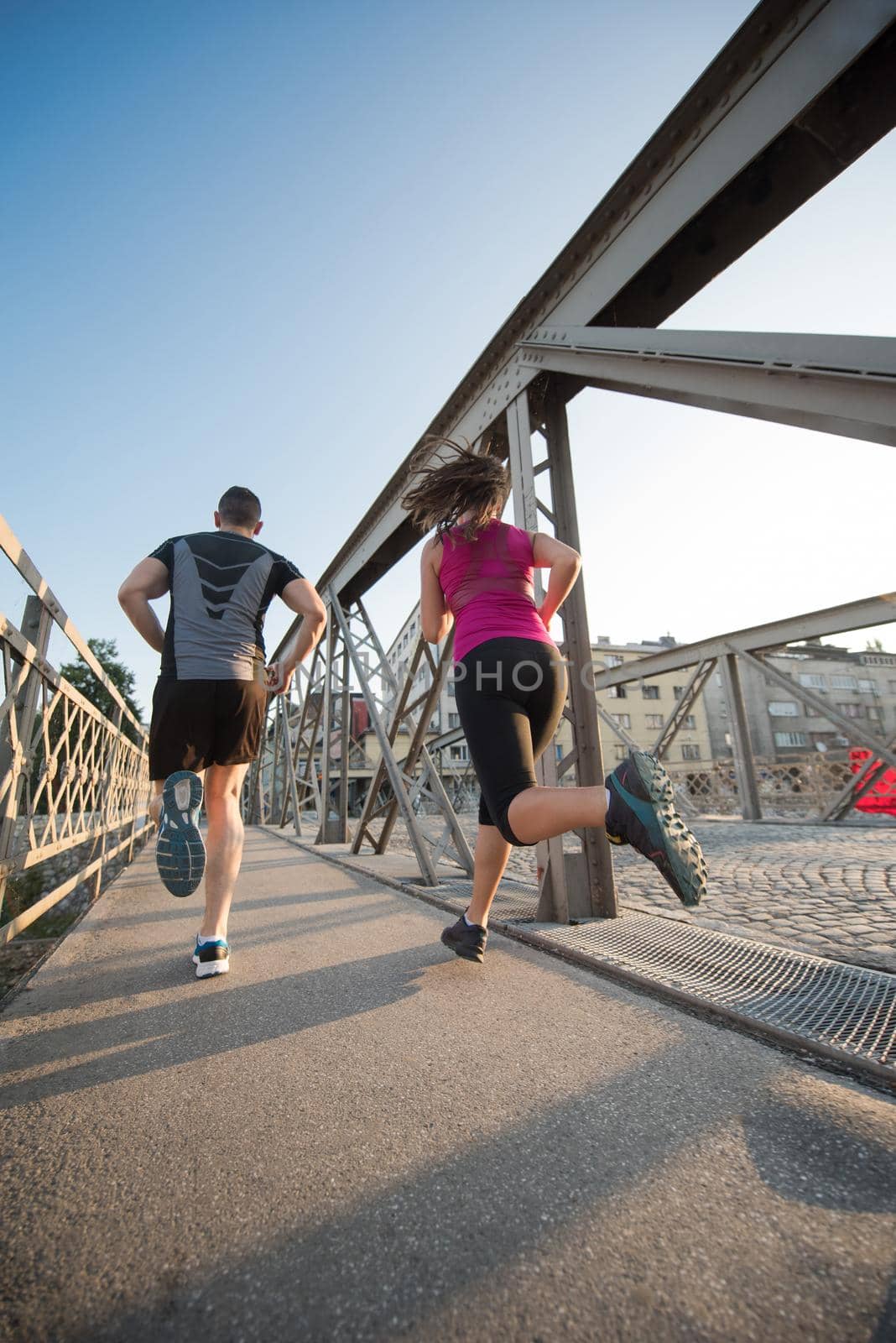 urban sports, healthy young couple jogging across the bridge in the city at sunny morning