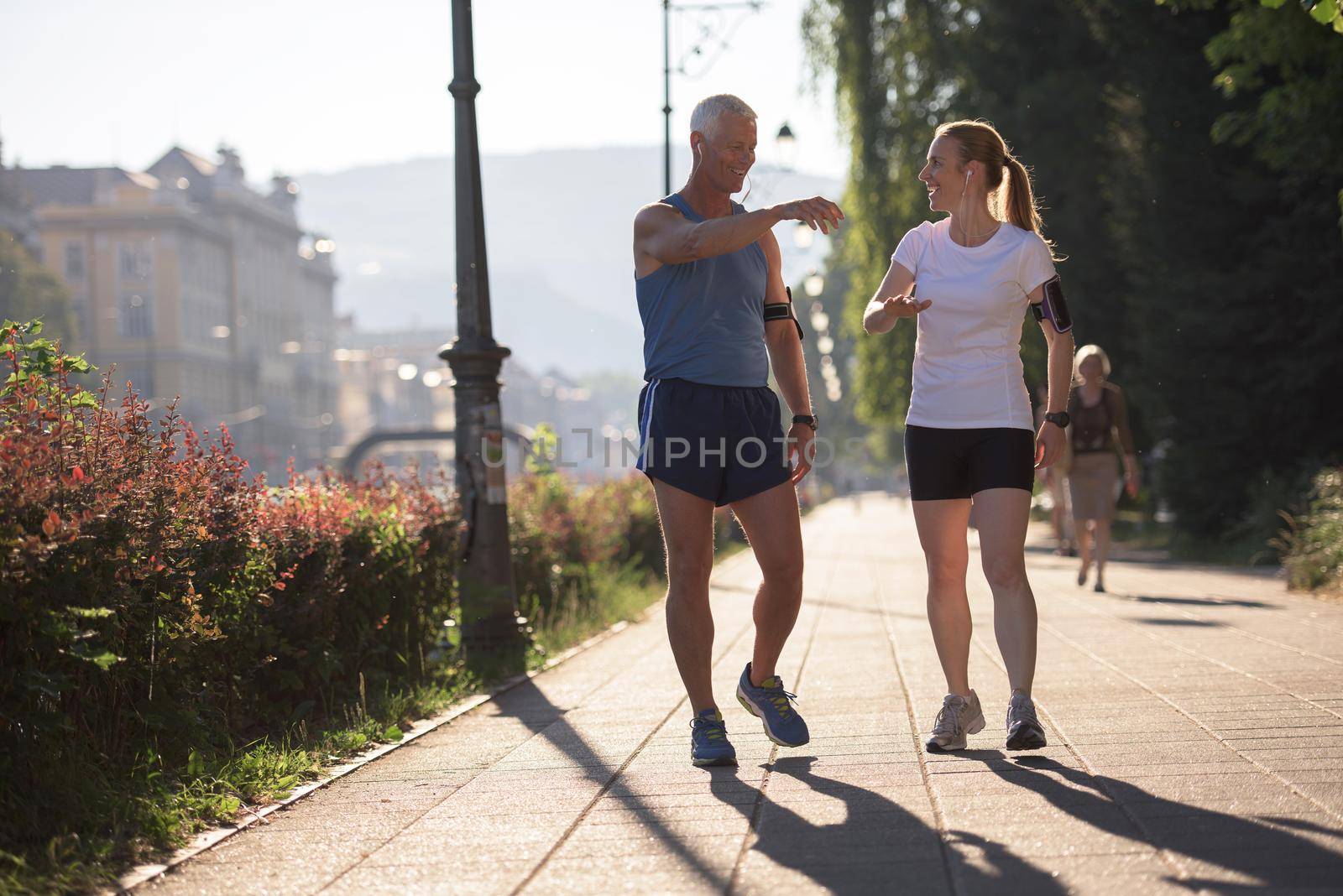 jogging couple check music playlist on phone and plan route before morning running workout  with sunrise in the city  and sun flare in background