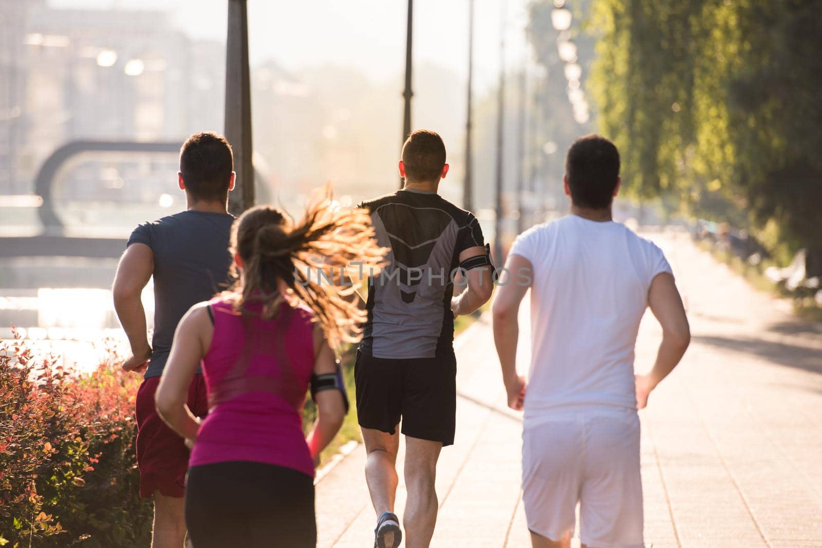 group of young sporty people jogging at sunny morning in the city