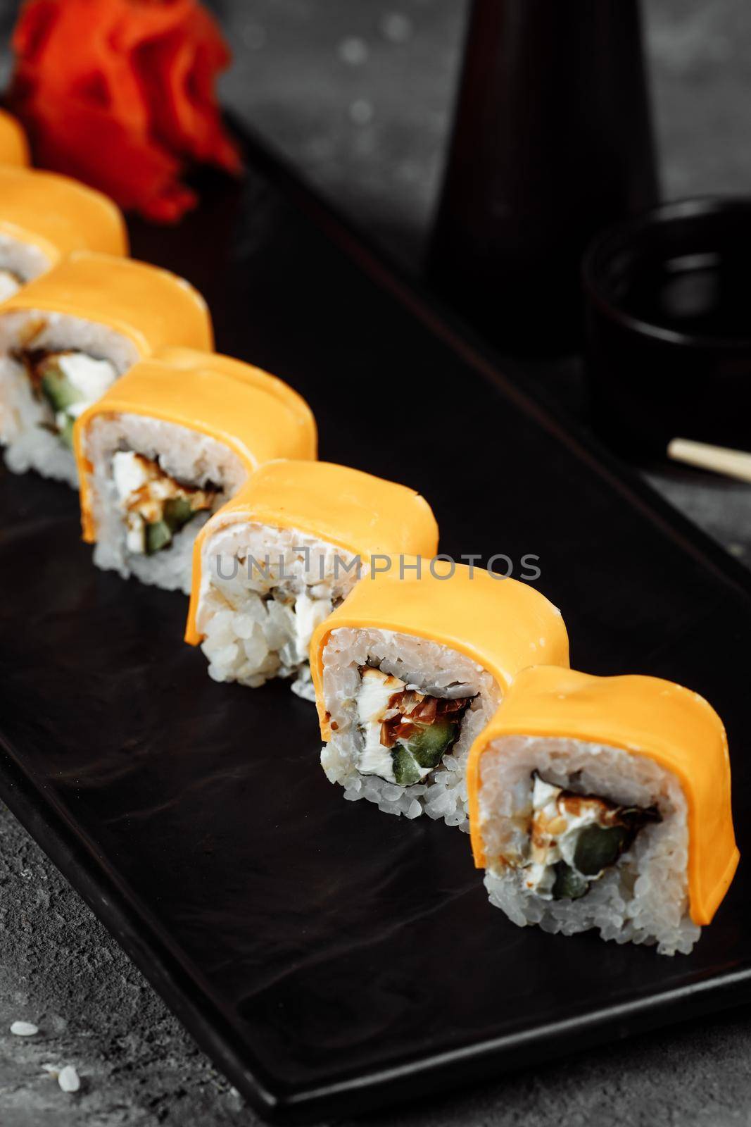 Traditional fresh japanese sushi rolls on a black stone Teka Kaji. Roll ingredients: cheese cheder, philadelphia cheese, cucumber, tuna chips, nori, rice by UcheaD
