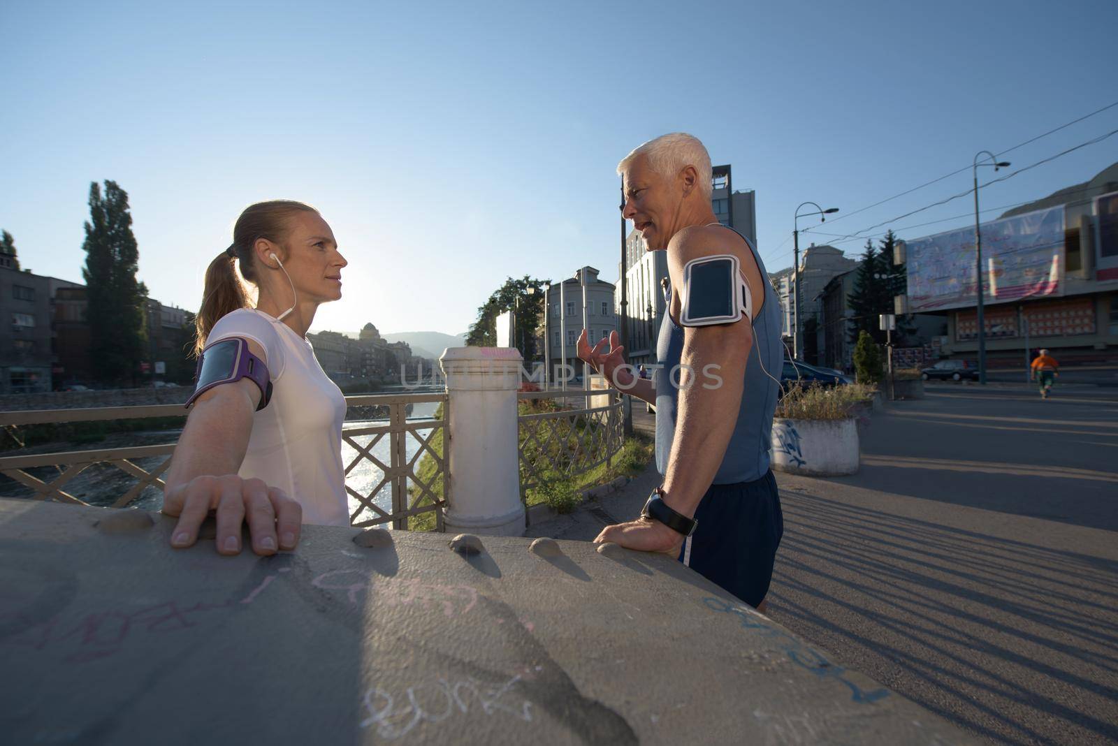 jogging couple check music playlist on phone and plan route before morning running workout  with sunrise in the city  and sun flare in background