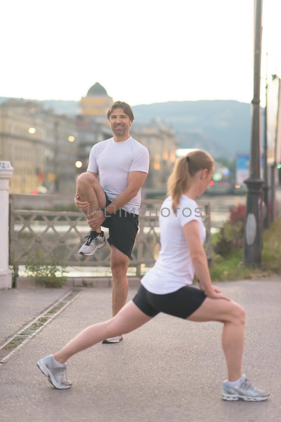 jogging couple warming up and stretching before morning running in the city