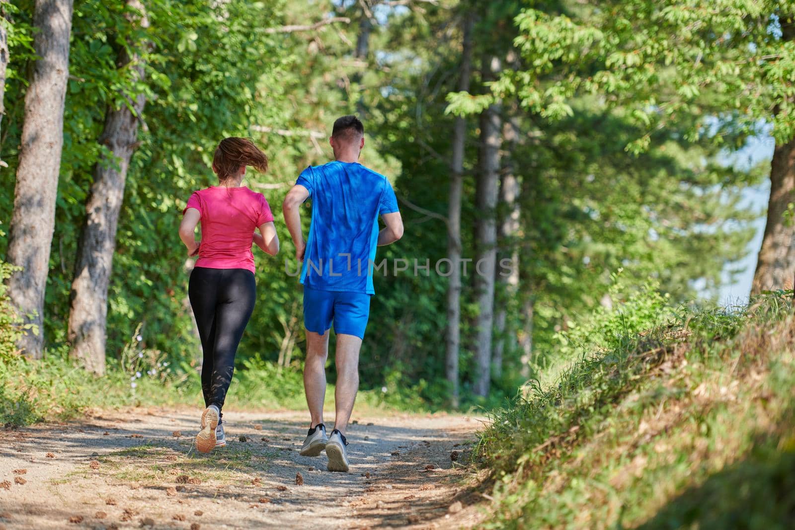 young happy couple enjoying in a healthy lifestyle while jogging on a country road through the beautiful sunny forest, exercise and fitness concept