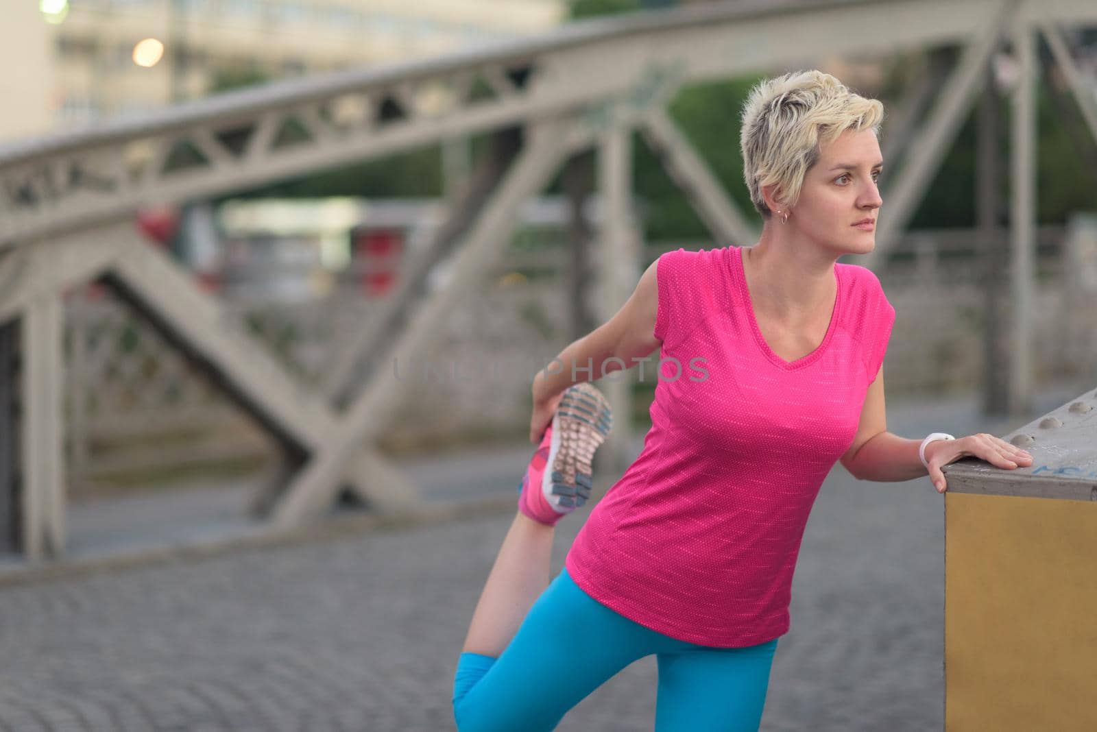 Fit blonde runner   woman warming up and stretching before morning jogging