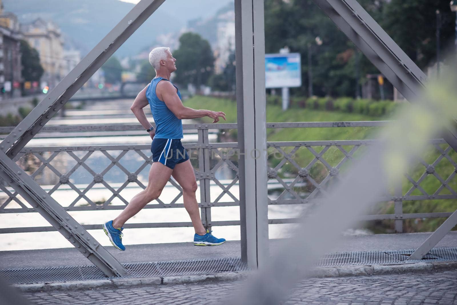 handsome senior man athlete jogging and  have morning workout with sunrise and city in background