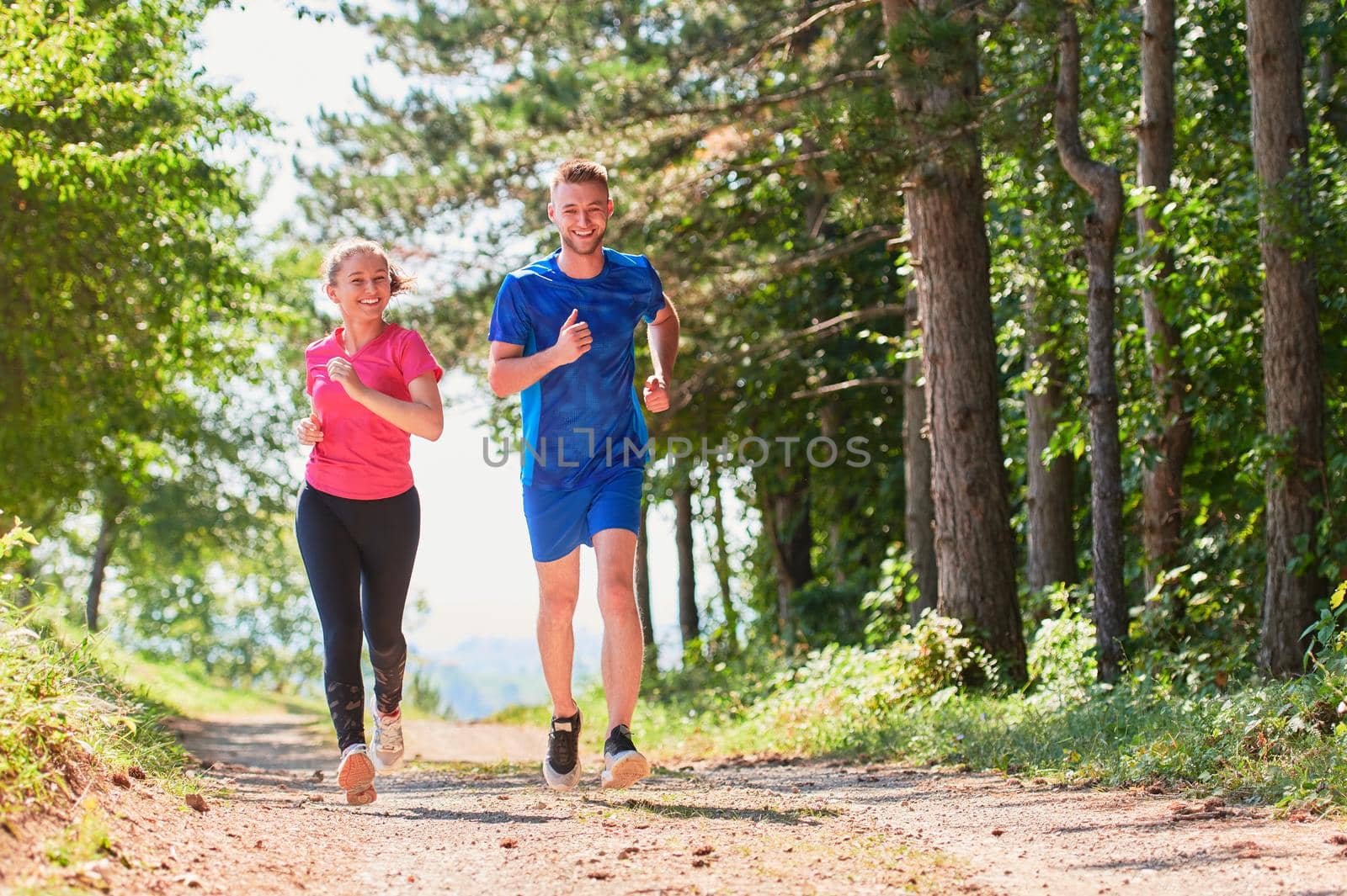 young happy couple enjoying in a healthy lifestyle while jogging on a country road through the beautiful sunny forest, exercise and fitness concept