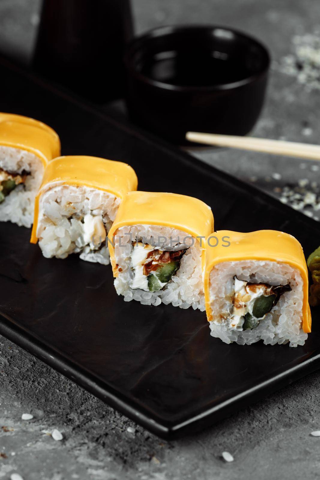 Traditional fresh japanese sushi rolls on a black stone Teka Kaji. Roll ingredients: cheese cheder, philadelphia cheese, cucumber, tuna chips, nori, rice.