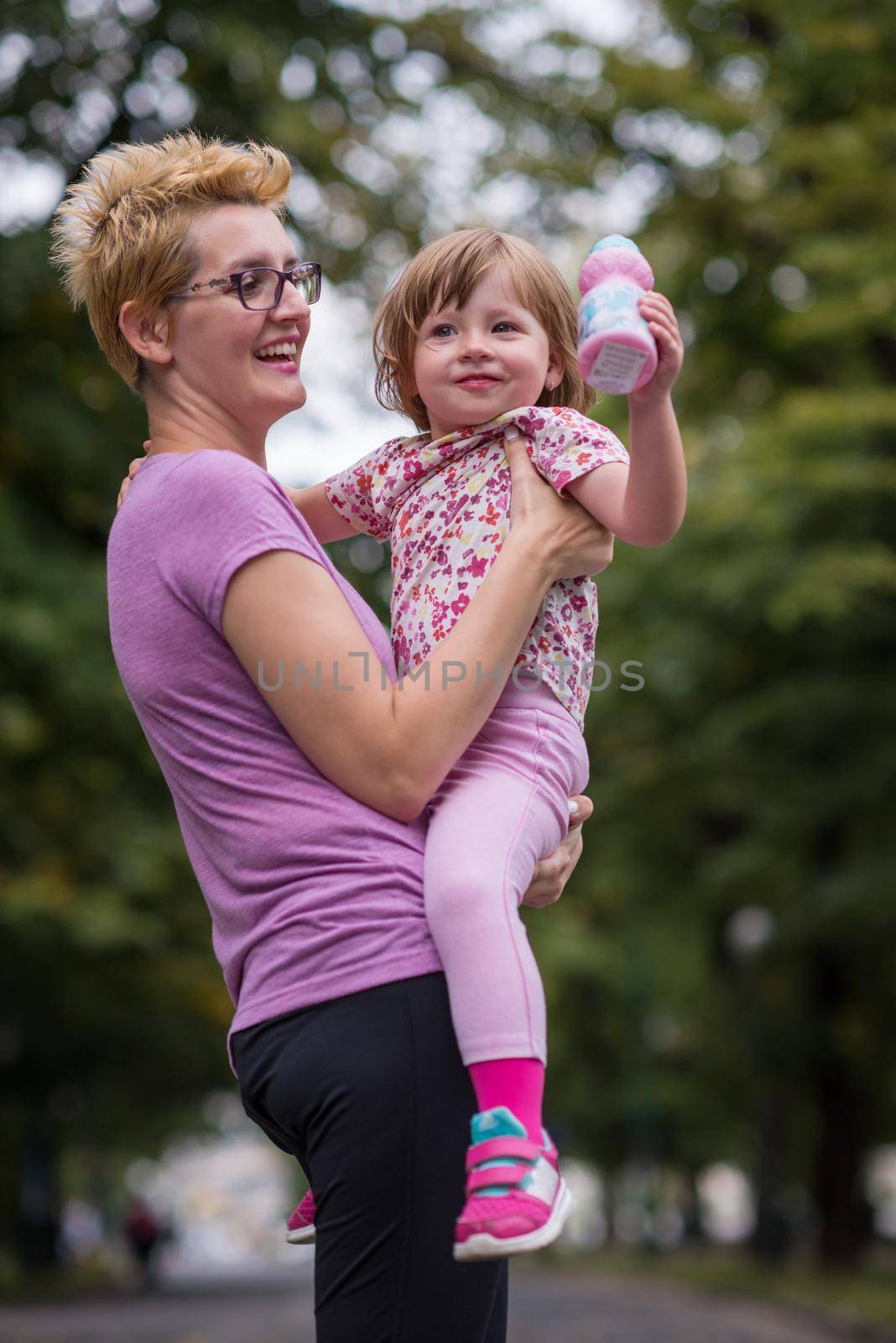 young sporty mother carries little daughter in arms while jogging in a city park,outdoor sports and fitness