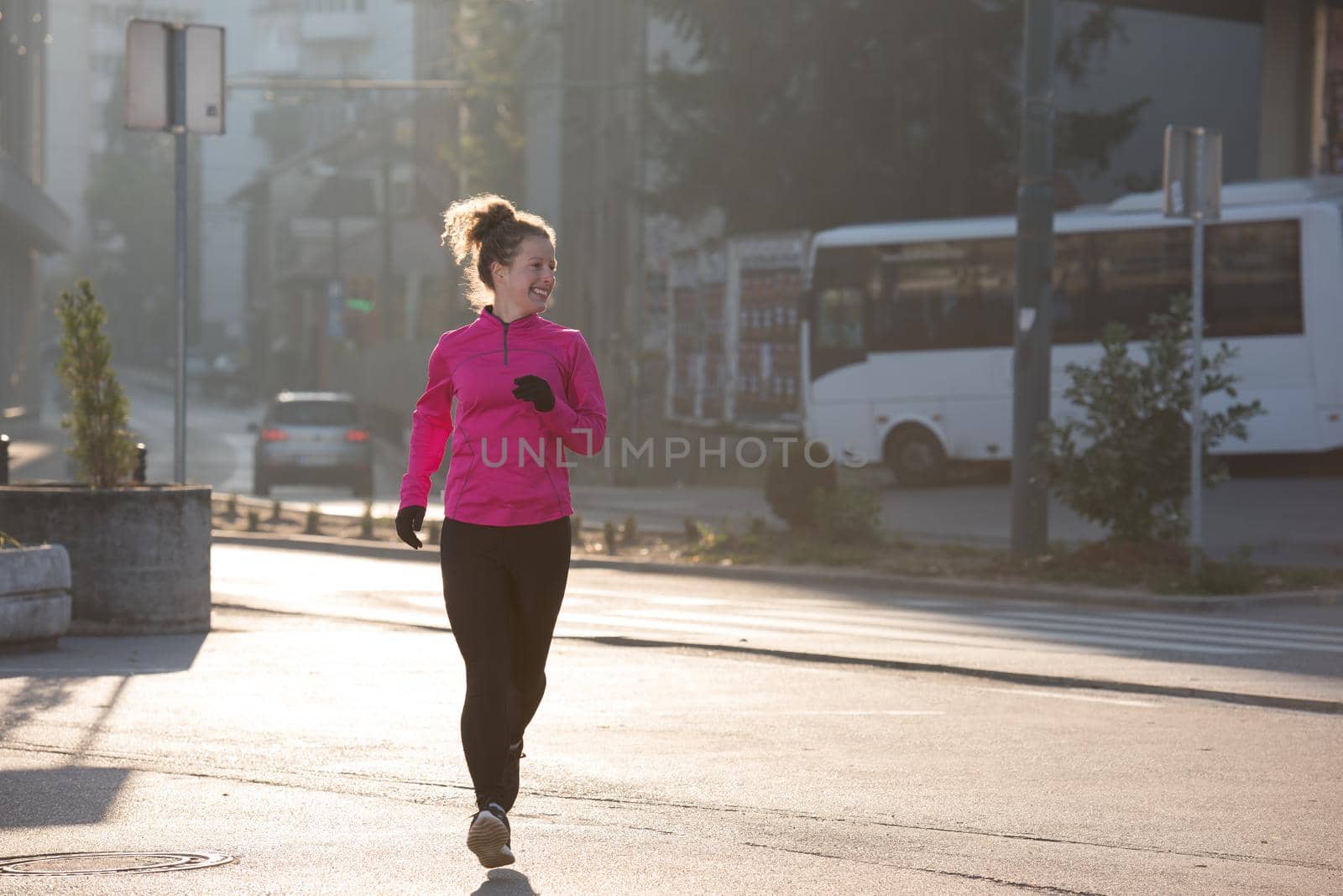 sporty woman running on sidewalk at early morning jogging with city  sunrise scene in background
