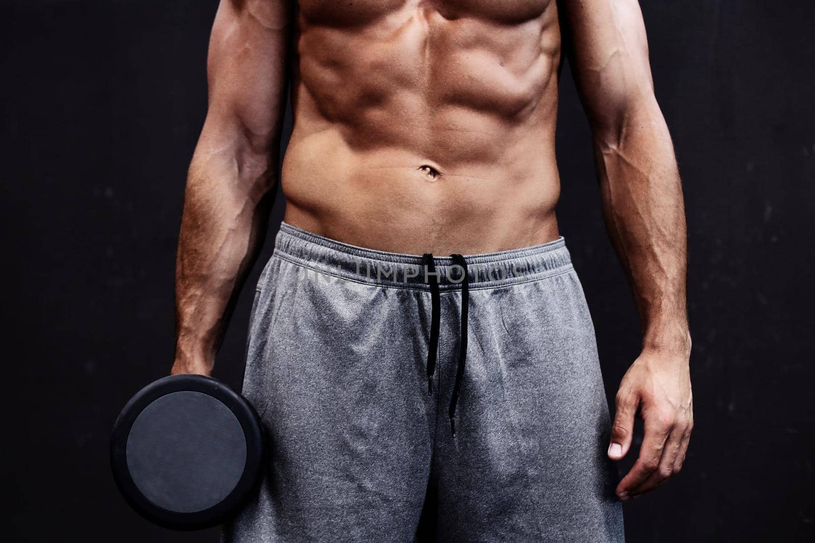 Close up of muscular bodybuilder guy doing exercises with weights over grey background. Black and white