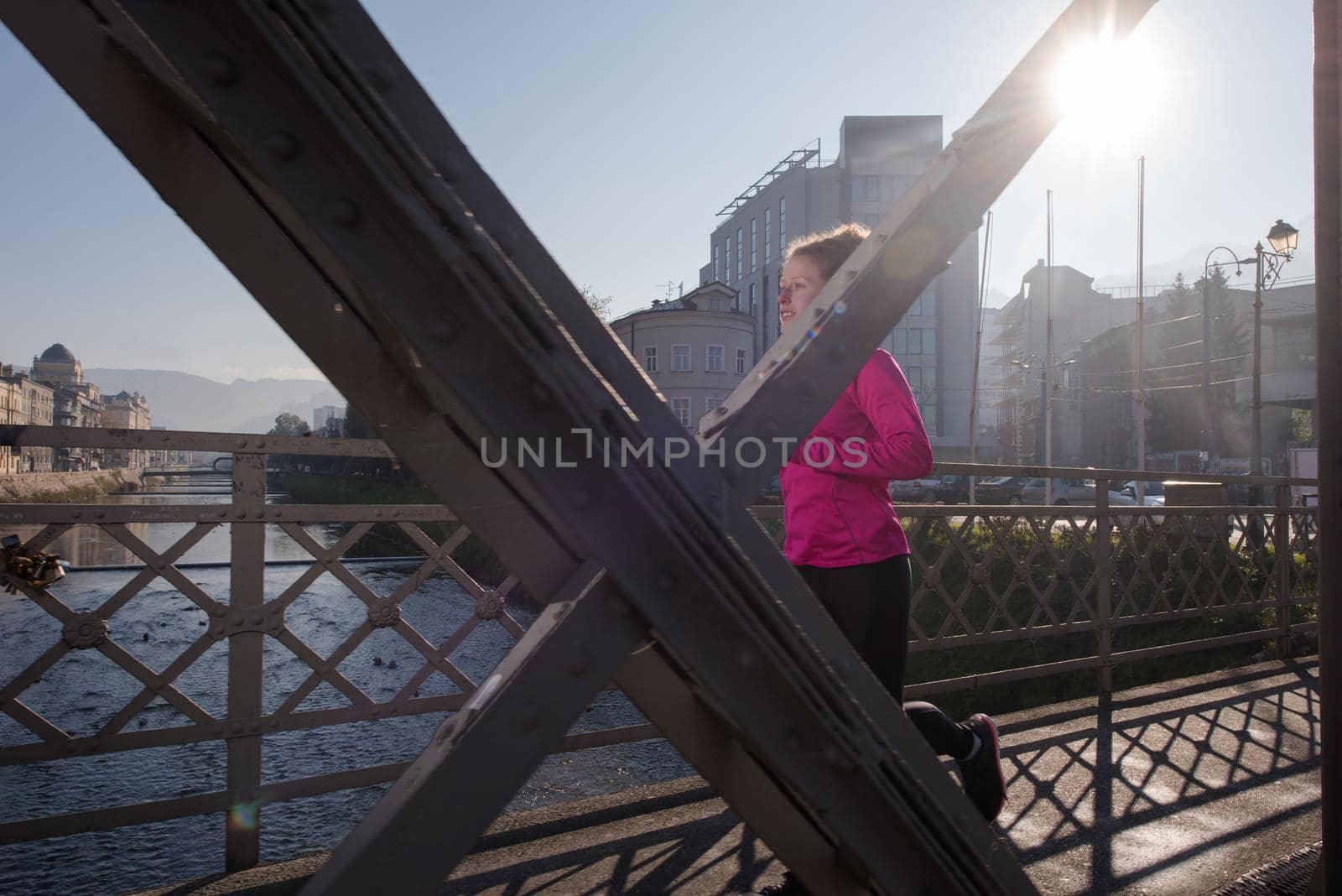 sporty woman running on sidewalk at early morning jogging with city  sunrise scene in background