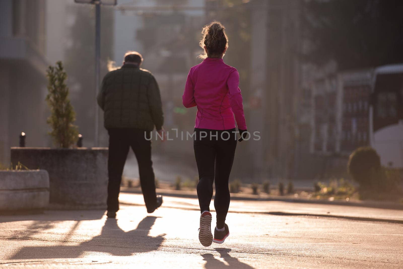 sporty woman running on sidewalk at early morning jogging with city  sunrise scene in background