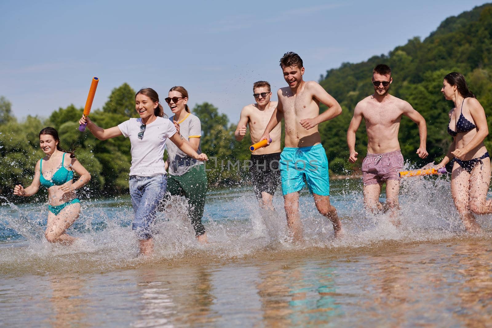 Summer joy group of happy friends having fun while running and splashing on river