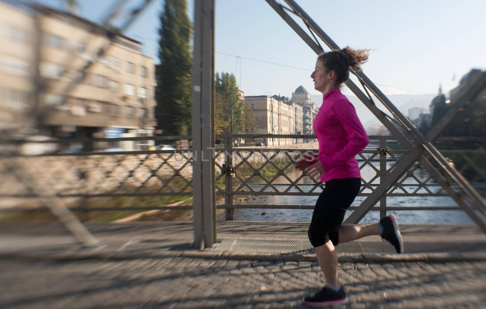 sporty woman running on sidewalk at early morning jogging with city  sunrise scene in background