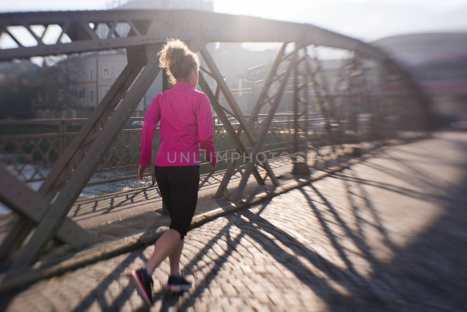 sporty woman running on sidewalk at early morning jogging with city  sunrise scene in background